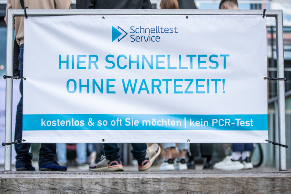 Menschen stehen vor einem Testzentrum an einem Transparent mit der Aufschrift "Hier Schnelltest - Ohne Wartezeit" an.