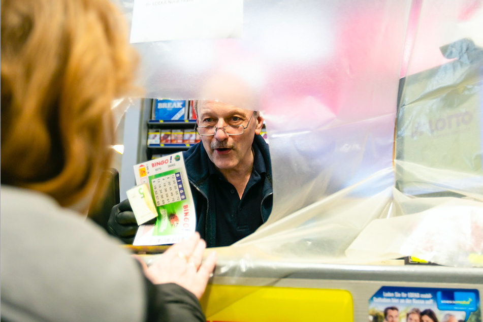 Ein Supermarkt-Mitarbeiter spricht mit einer Kundin durch eine Plastikfolie hindurch.
