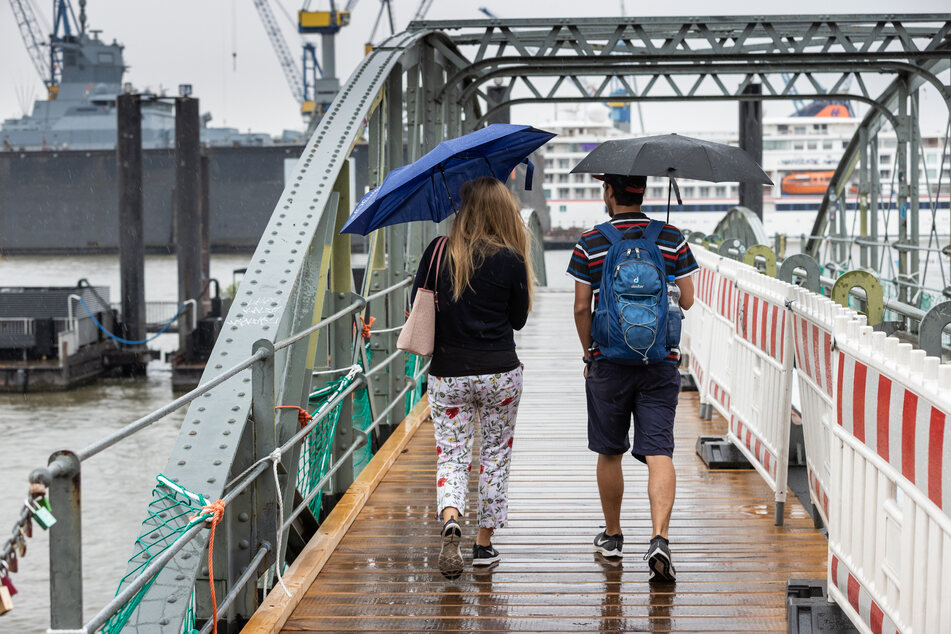 Mit Regenschirmen schützen sich eine Frau und ein Mann bei einem Spaziergang im Hamburger Hafen.