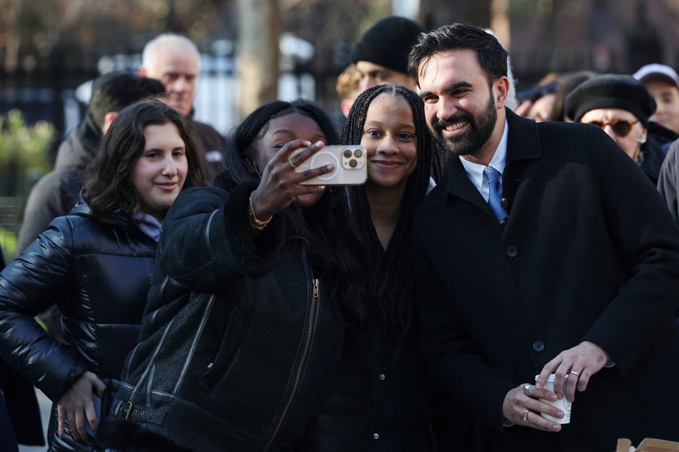 New York City Mayor-elect Zohran Mamdani (r.) poses for a selfie with supporters as he hands out hot cocoa at Stuyvesant Square Park on December 4, 2025.