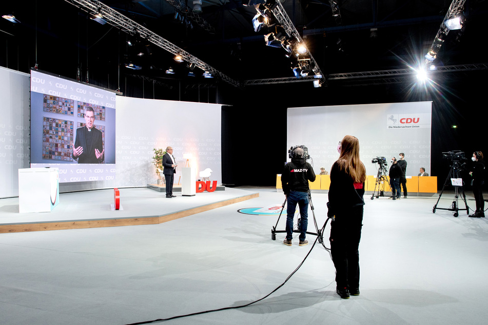 Bernd Althusmann (54, l.) steht im Rahmen des Landesparteitags in einem TV-Studio, während Bischof Heiner Willmer (auf dem Bildschirm) ein geistliches Grußwort hält.