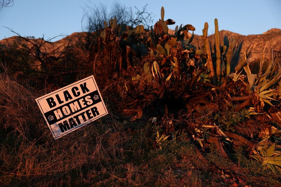 A "Black Homes Matter" sign is displayed next to burned vegetation in front of the empty lot of a destroyed home on East Loma Alta Drive in Altadena, California, on December 29, 2025.
