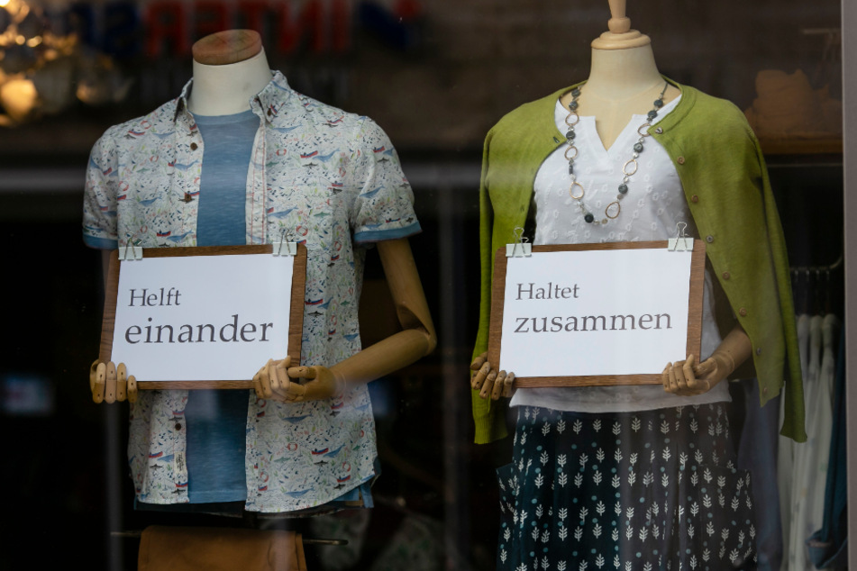 Schaufensterpuppen eines Bekleidungsgeschäftes in der Flensburger Innenstadt halten Schilder mit der Aufschrift "Helft einander" und "Haltet zusammen".