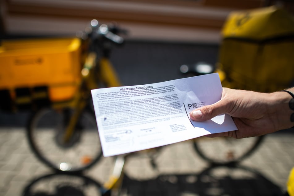 Ein Briefträger der Deutschen Post hält eine Wahlbenachrichtigung in der Hand. Stimmzettel können bis spätestens zwei Tage vor der Wahl bestellt werden. (Symbolbild)