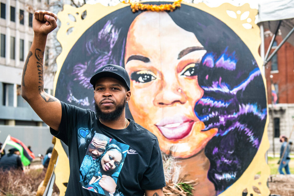 Breonna Taylor's boyfriend Kenneth Walker poses in front of her painted portrait on the one-year anniversary of her shooting.