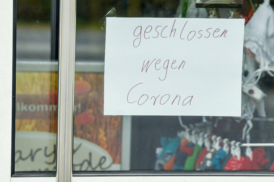 Ein Zettel mit der Aufschrift "geschlossen wegen Corona" klebt an der Eingangstür zu einem Einzelhandelsgeschäft in Brandenburg. (Archivbild)
