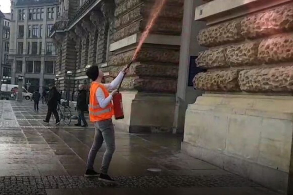 Einer der Aktivisten der Gruppierung "Letzte Generation" entleert den Inhalt eines mit Farbe gefüllten Feuerlöschers am Donnerstagvormittag an der Fassade des Hamburger Rathauses.