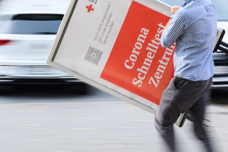 Ein Mitarbeiter des DRK Dresden trägt ein Hinweisschild für ein Corona Schnelltest Zentrum nach dem Abbau der Teststelle weg.