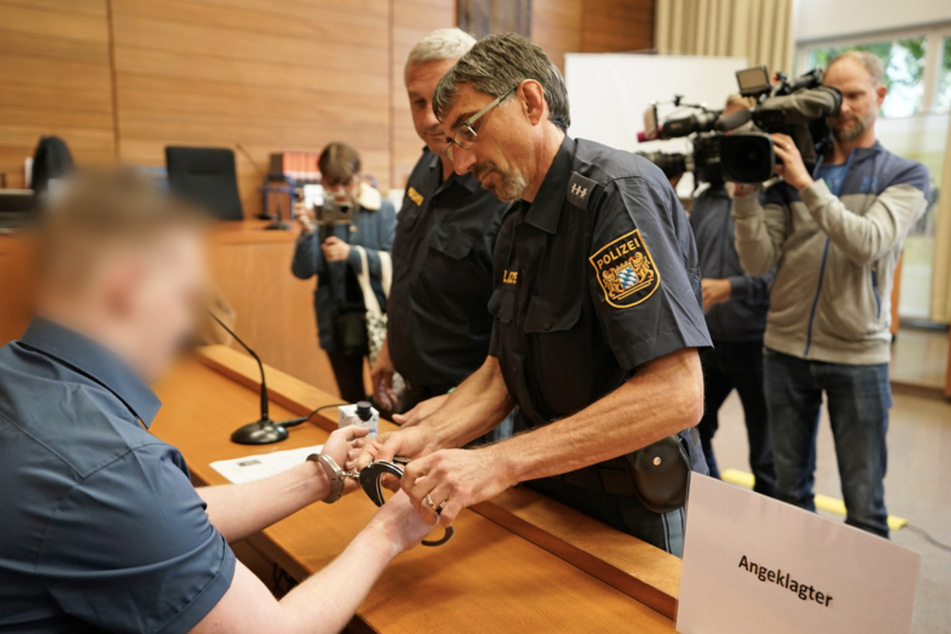 Justizbeamte nehmen dem Angeklagten im Landgericht Traunstein vor Prozessbeginn die Handschellen ab.