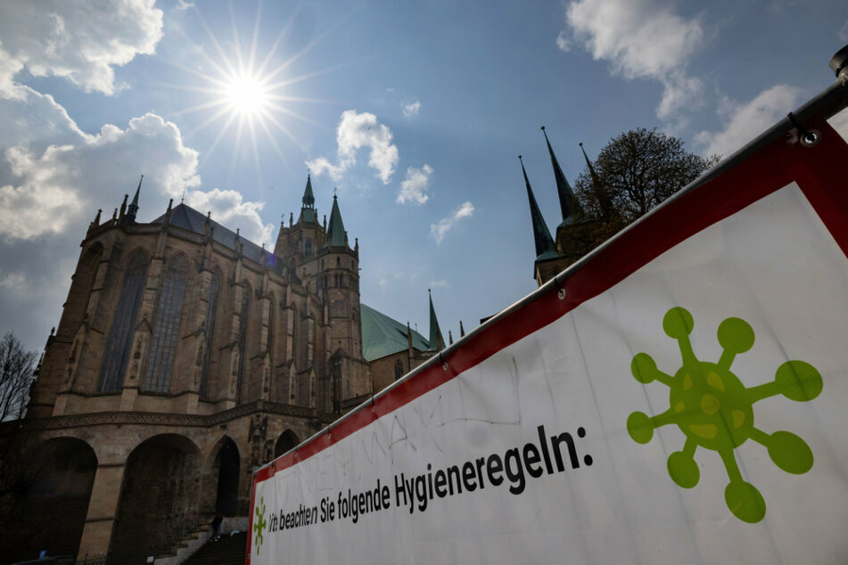 Ein großes Schild weist auf dem Erfurter Domplatz auf die Corona-Regeln hin. Die Sieben-Tage-Inzidenz in Thüringen weiter auf einem Abwärtstrend.