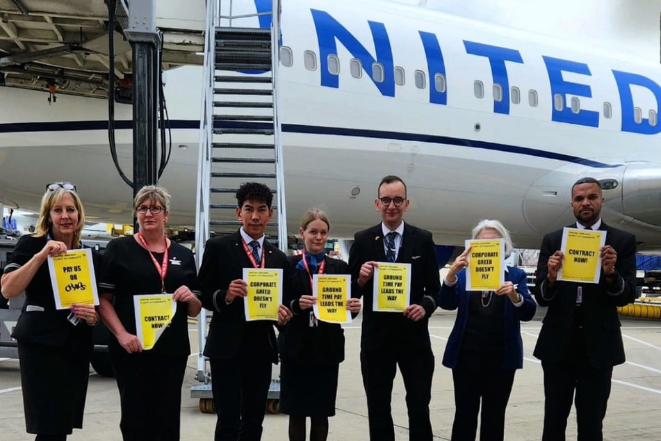 United flight attendants hold signs reading "Pay us or chaos" And "Corporate greed is not acceptable" after landing in London, UK.