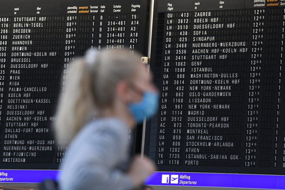 Eine Frau, die einen Mundschutz trägt, steht im Terminal 1 des Frankfurter Flughafens in der Abflughalle vor einer großen Anzeigetafel. Am größten deutschen Airport öffnet nun das erste Corona-Testzentrum an einem Flughafen in Deutschland.