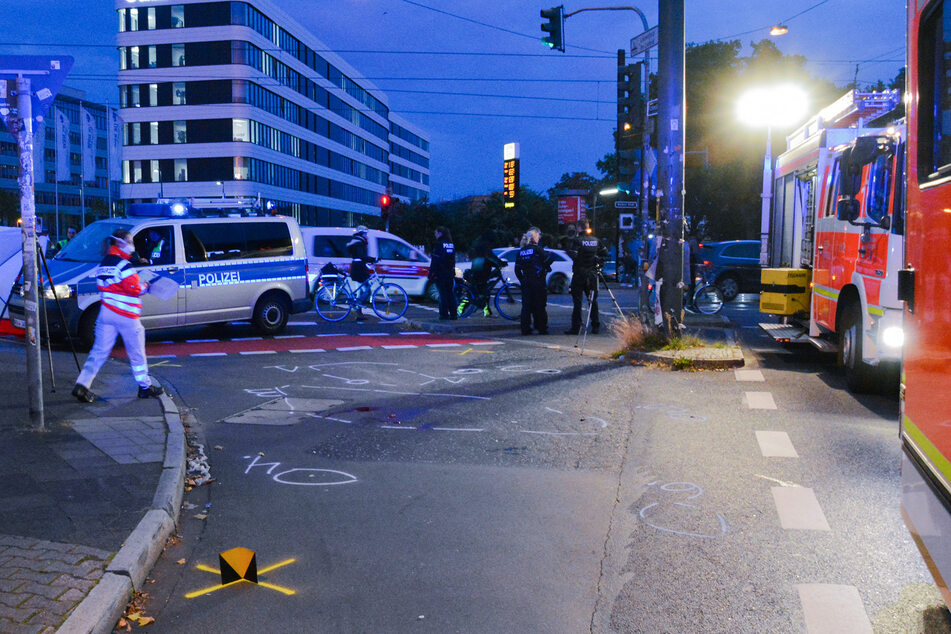 Polizei und Krankenwagen stehen an einer Unfallstelle, wo Markierungen auf der Straße zu sehen sind.