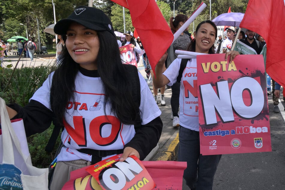 Women hold signs during a march calling on people to vote NO in the referendum proposed by Ecuador's President Daniel Noboa, in Quito on November 12, 2025.