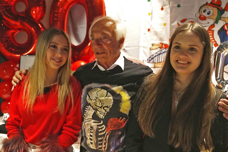 Der 80-jährige Reinhold hält an seinem Geburtstag seine zwei Enkelinnen im Arm.