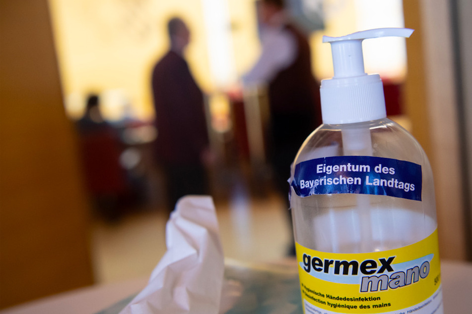 Eine Flasche mit Desinfektionsmittel und der Aufschrift "Eigentum des Bayerischen Landtags" steht während einer Plenarsitzung im bayerischen Landtag am Eingang des Plenarsaals.