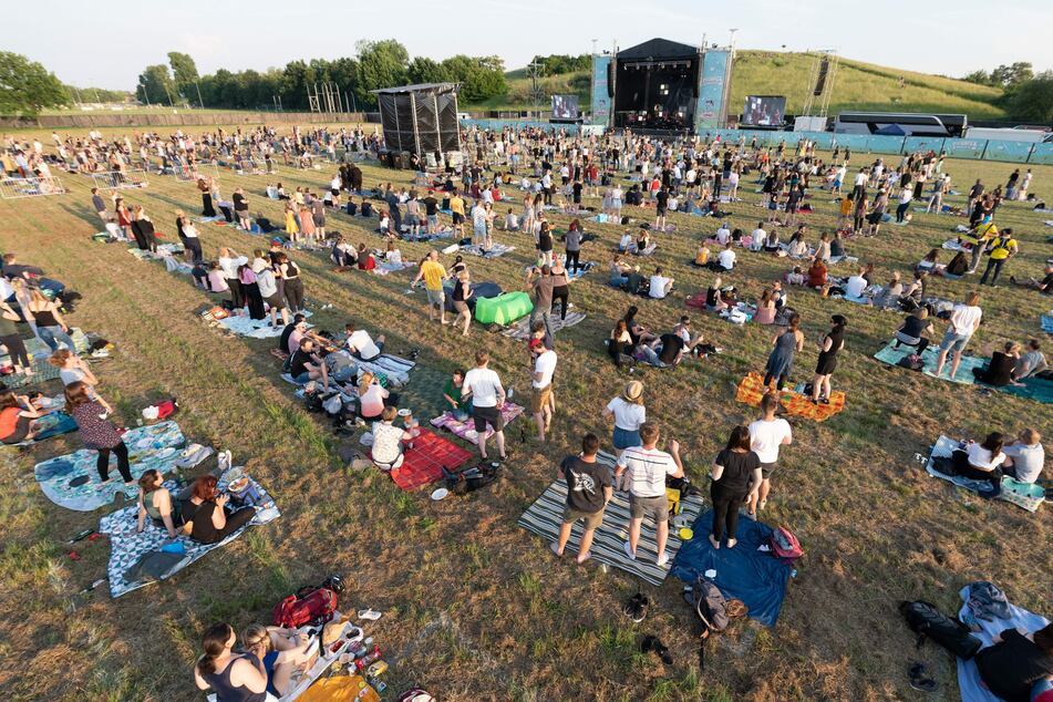 Die Zuschauer stehen und sitzen während eines Konzerts der Band Meute, das in der Reihe "Picknick-Konzerte" auf dem Messegelände stattfindet, mit Abstand auf der Wiese.