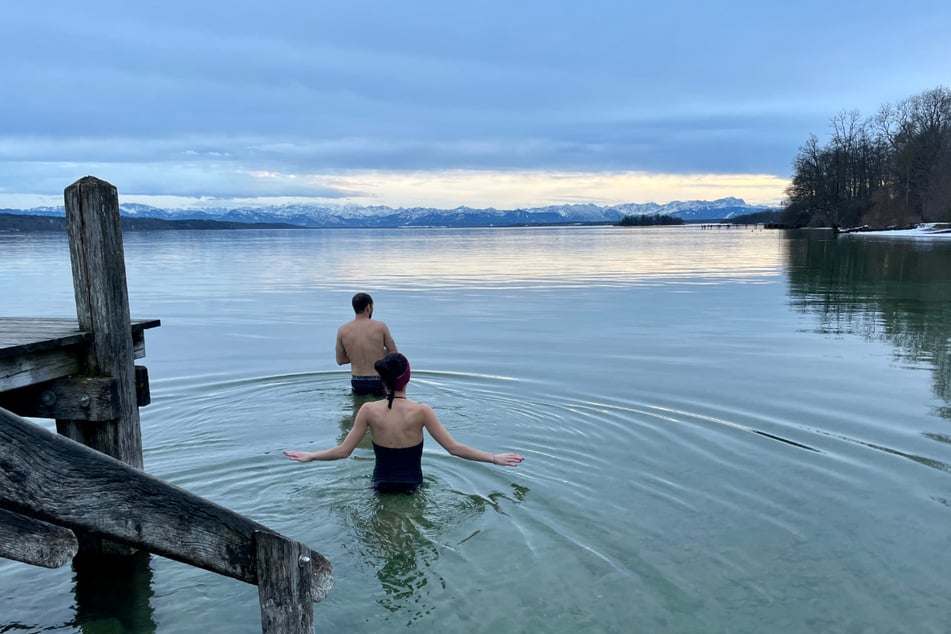 Die Geschwister Tim und Sabrina gehen vor dem Panorama der schneebedeckten bayerischen Alpen im Starnberger See baden.
