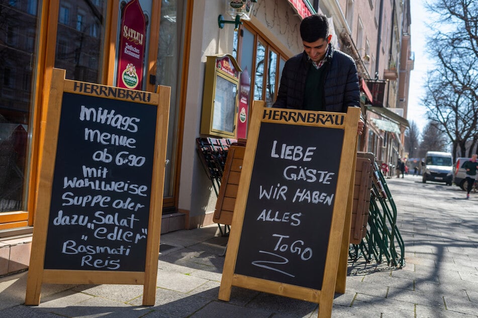 Ein indischer Koch stellt Schilder vor sein Restaurant im Stadtteil Haidhausen.