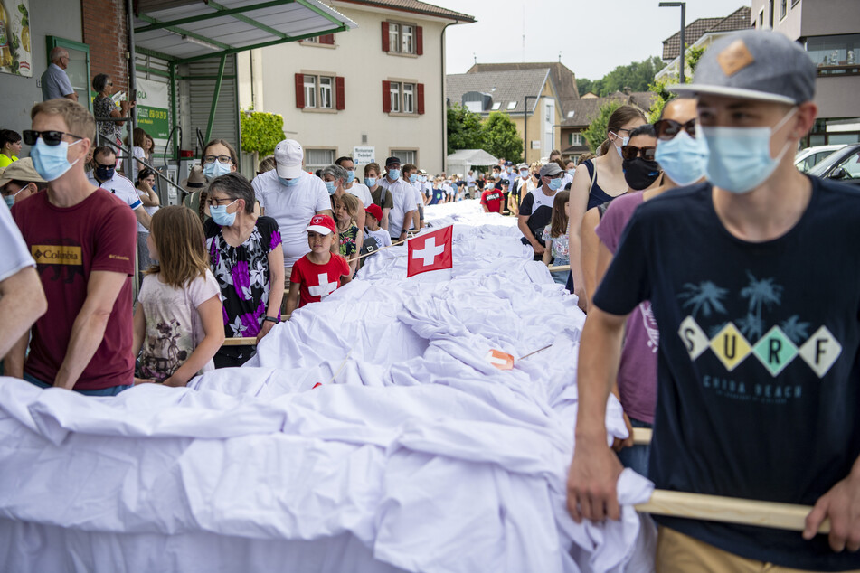 Zahlreiche Menschen tragen ein Hosenbein der überdimensional großen Hose zum Ort der Präsentation.