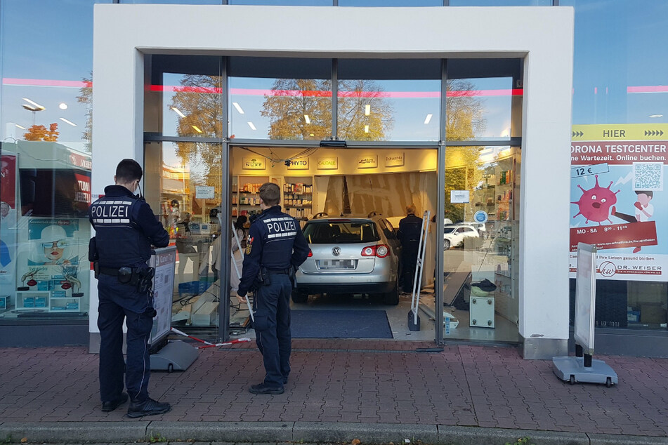 Polizisten stehen an der Unfallstelle. Ein 70-jähriger Fahrer krachte in eine Apotheke.