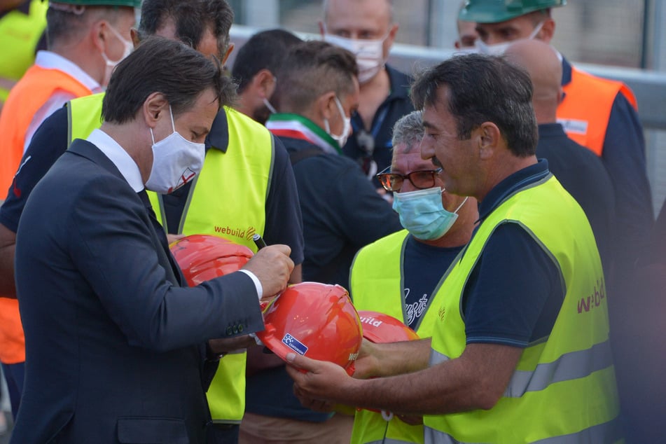 Genua: Giuseppe Conte (l), Ministerpräsident von Italien, unterschreibt den Helm eines Bauarbeiters während der Einweihungsfeier der Brücke San Giorgio. (Archivbild)
