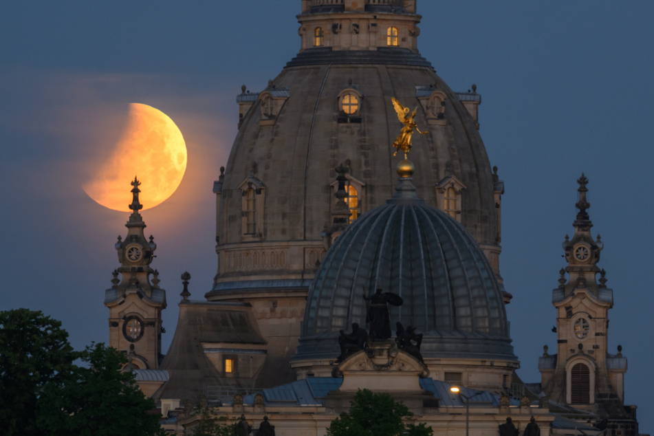 Der Mond geht am Morgen während einer partiellen Mondfinsternis hinter der Frauenkirche und der Kuppel der Kunstakademie mit dem Engel "Fama" unter.