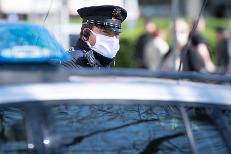 Ein Polizist steht vor seinem Streifenwagen und trägt einen Mundschutz.