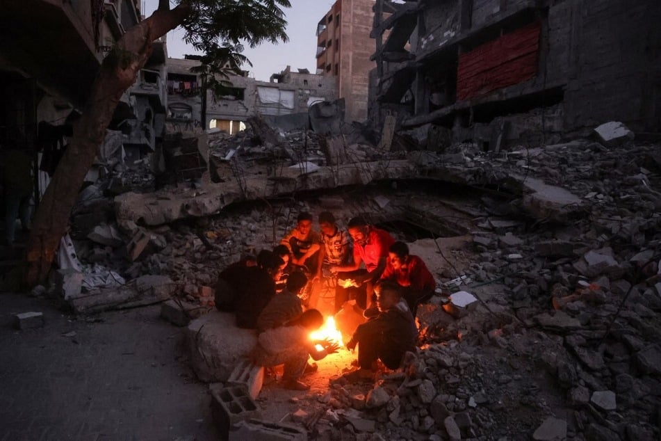 Palestinians sit around a bonfire amid destroyed buildings in the Bueij refugee camp in the central Gaza Strip.