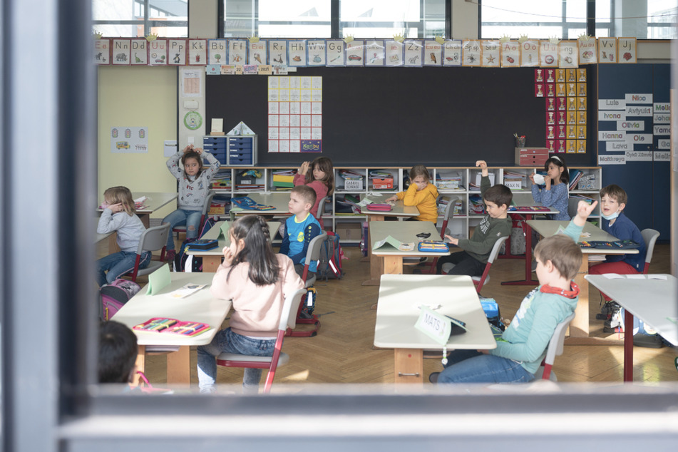 Kinder sitzen in einer ersten Klasse an einer Grundschule mit Wechselunterricht hinter einem offenen Fenster.
