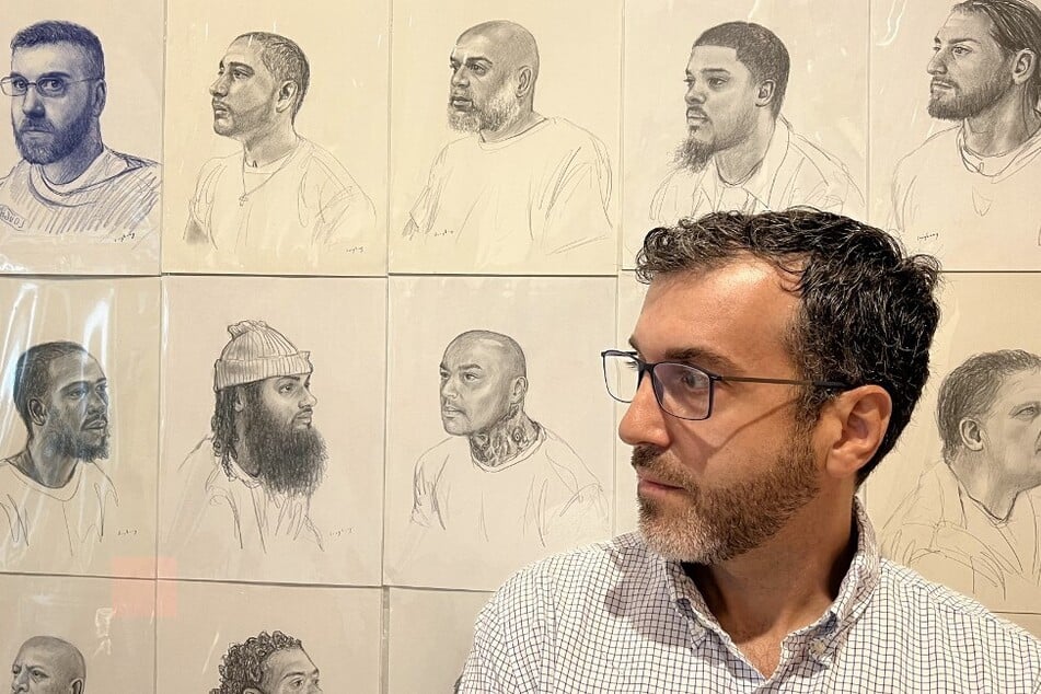 Artist Mark Loughney stands in front of his piece Pyrrhic Defeat: A Visual Study of Mass Incarceration displaying hundreds of portraits of incarcerated men he made while in prison himself.