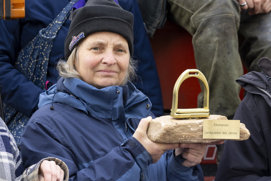 Milana Müller (54) mit dem "Landgrapscher des Jahres". Die Form eines Steigbügels für den Preis ist bewusst gewählt und kritisiert CDU und Bauernverband als Steigbügelhalter für Investoren, die den Flächenausverkauf vorantreiben.