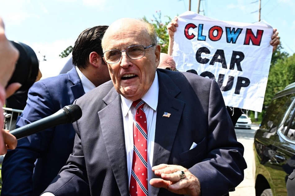 A person holds a "Clown Car Coup" sign as Rudy Giuliani speaks to the media after being booked, outside the Fulton County Jail in Atlanta, Georgia, on August 23, 2023.
