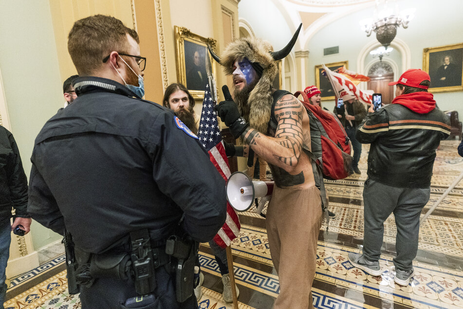 Jacob C. und andere Unterstützer von US-Präsident Trump stehen auf dem Gang vor der Senatskammer im US-Kapitol und diskutieren mit einem Polizisten des Kapitols. Unter den Eindringlingen sind auch Anhänger der rechten "QAnon"-Verschwörungstheorie gewesen.