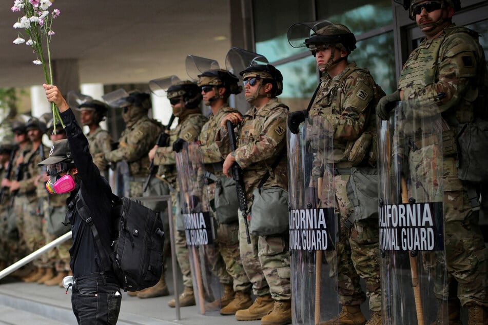 A demonstrator raises his hand holding flowers as members of the National Guard stand in formation outside a federal building during the No Kings protest against President Donald Trump's policies in Los Angeles, California, on June 14, 2025.