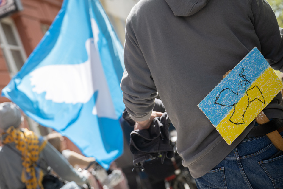 Ein Mann, der ein Schild mit den Nationalfarben der Ukraine und einer Friedenstaube am Gürtel befestigt hat, nimmt in Frankfurt am Main an einem Ostermarsch teil.