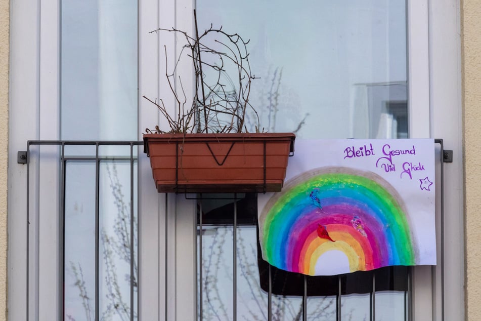 Ein großes Blatt Papier mit einem Regenbogen und der Aufschrift "Bleibt Gesund - Viel Glück" hängt an einem Fenster in München.