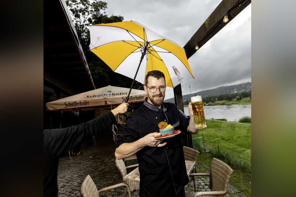 In der "Feuchten Kurve" müssen die Mitarbeiter auch mal mit Regenschirm in der Hand arbeiten. Hier zu sehen: Koch Nico Bombach (43) mit einer guten Portion Würzfleisch und einem frisch gezapften Bier.