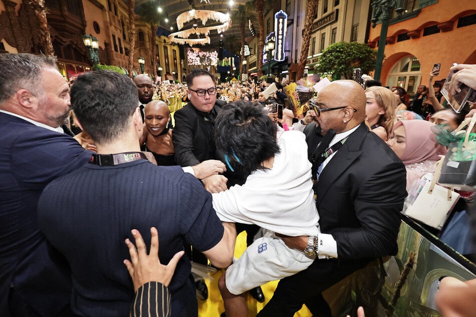 A man accused of attacking Ariana Grande is grabbed by security guards as co-star Cynthia Erivo reacts at the premiere of their film Wicked: For Good in Singapore.