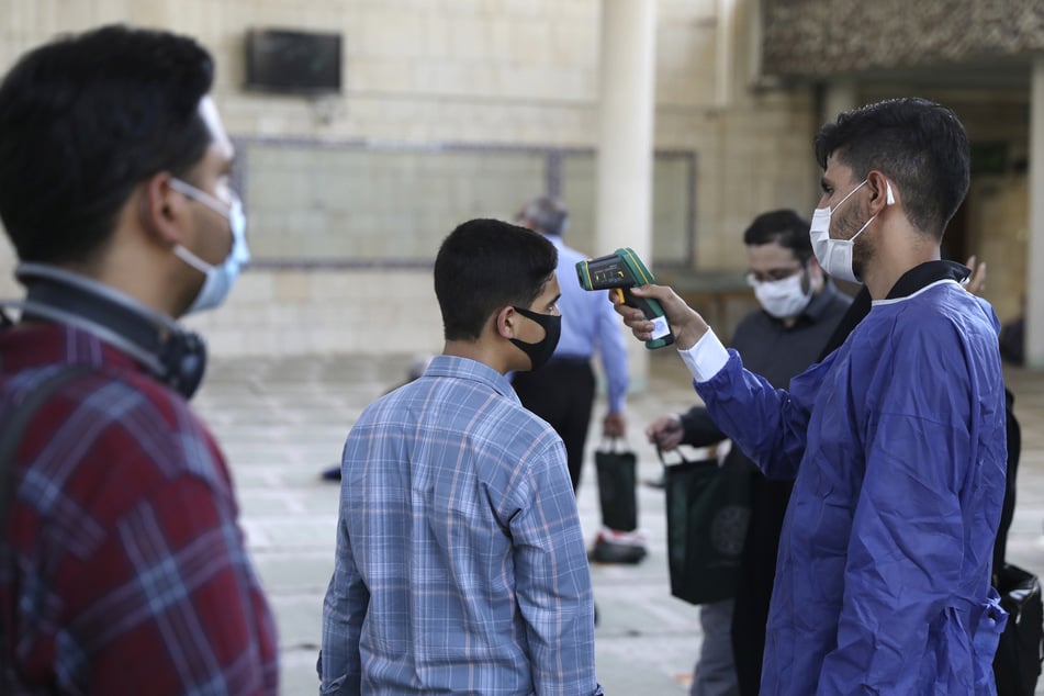 Ein Freiwilliger (r.) misst die Temperatur eines gläubigen Iraners, der die Moschee der Universität Teheran zum Gebet betritt. Touristen kommen vorerst nicht mehr in den Iran. (Archvibild)