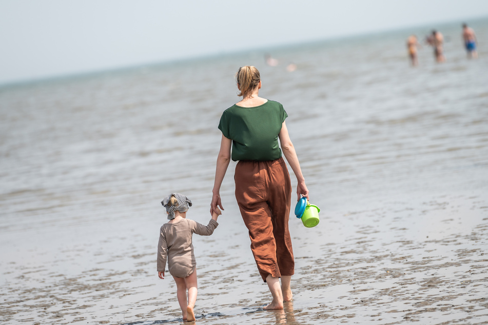 Eine Strandbesucherin ist bei sommerlichen Temperaturen mit ihrer Tochter am Nordseestrand von Schillig.