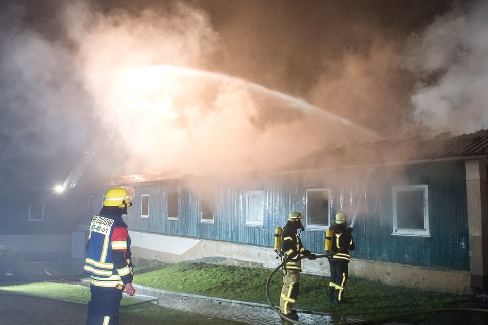 Die Einsatzkräfte der Feuerwehr löschen den Brand in der Flüchtlingsunterkunft. Die Brandursache ist noch unklar.