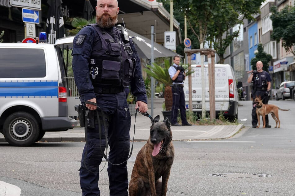 Ein Diensthundeführer steht in Essen mit seinem Polizeihund auf der Straße vor einer Bar.