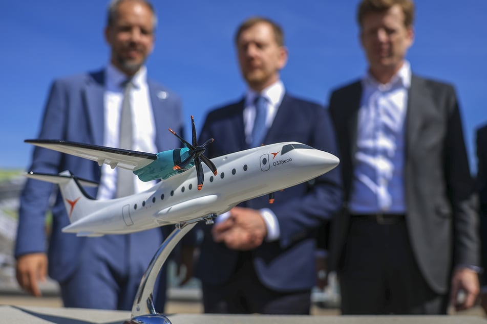 Nico Neumann (v.l.), Co-CEO Deutsche Aircraft, Michael Kretschmer (CDU), Ministerpräsident von Sachsen, und Götz Ahmelmann, CEO der Mitteldeutsche Flughafen AG, stehen im April 2025 hinter dem Flugzeugmodell der D328 Eco nach der Grundsteinlegung für ein neues Flugzeugwerk auf dem Flughafen Leipzig/Halle. (Archivbild)