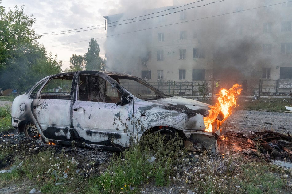 Ein Auto brennt vor dem Hintergrund eines beschädigten Wohnhauses nach einem russischen Raketenangriff in Charkiw.