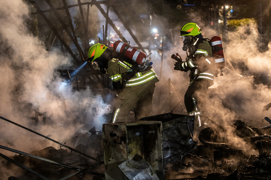 Feuerwehrleute bahnen sich ihren Weg durch die verbrannten Trümmer eines Wohnwagens.