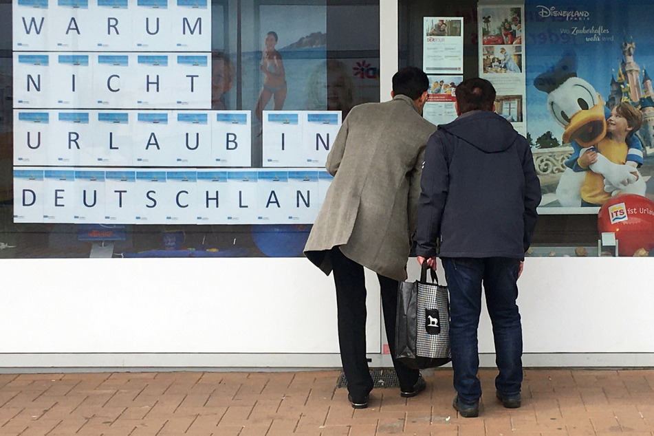 "Warum nicht Urlaub in Deutschland": Zwei Männer schauen in Dortmund in das Schaufenster eines Reisebüros.