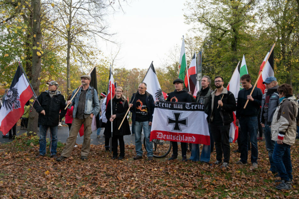 Teilnehmer einer Demonstration von Reichsbürgern tragen schwarzrotweiße und andere Fahnen. Ein Mann zeigt dabei eine Flagge mit der Aufschrift "Treue Um Treue - Deutschland".