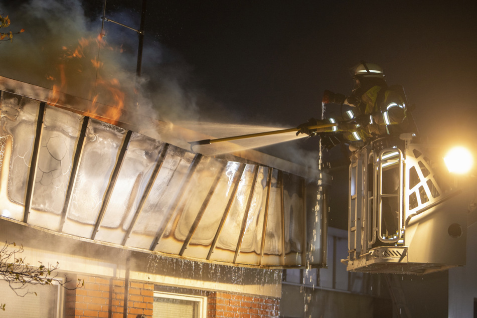 Feuerwehrleute löschen von einer Drehleiter aus den Dachbrand.