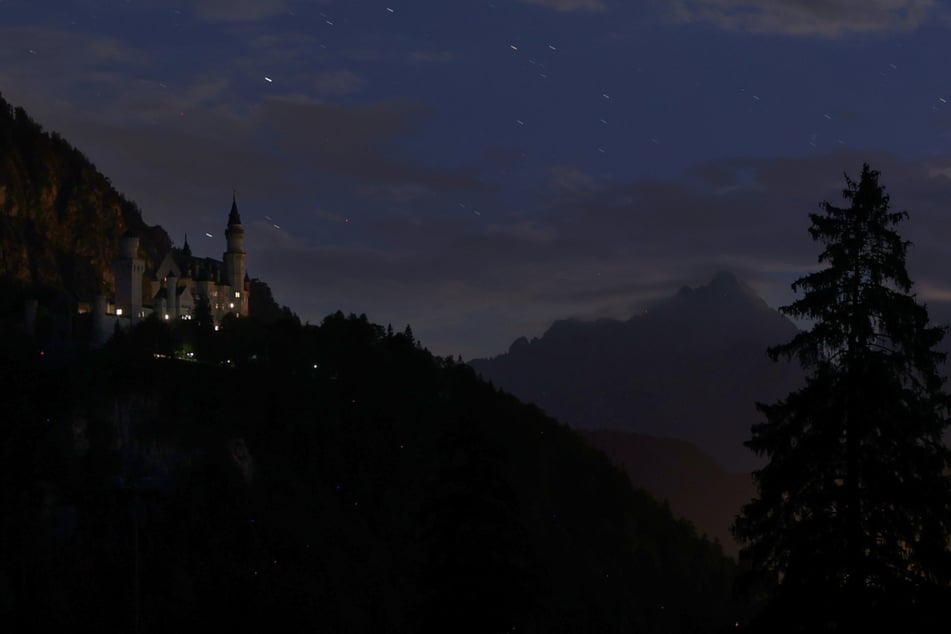 Schloss Neuschwanstein (l.) liegt in der Dunkelheit. Um Energie zu sparen, wird das Wahrzeichen nicht mehr von Scheinwerfern angestrahlt.